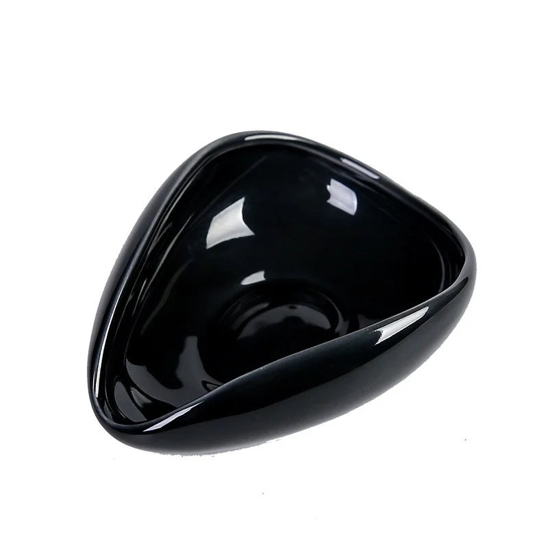 Glossy black ceramic coffee cupping bowl with rounded triangular shape on white background