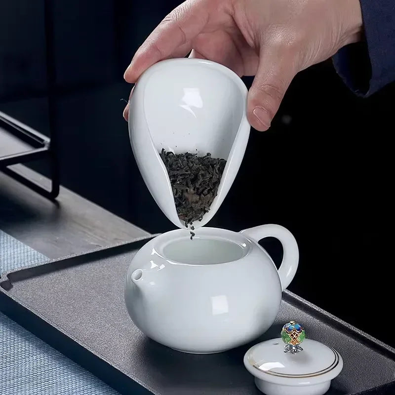Loose leaf tea being poured into a white ceramic teapot on a tray