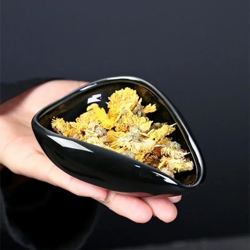 Hand holding a black ceramic bowl filled with dried yellow flowers against a dark background