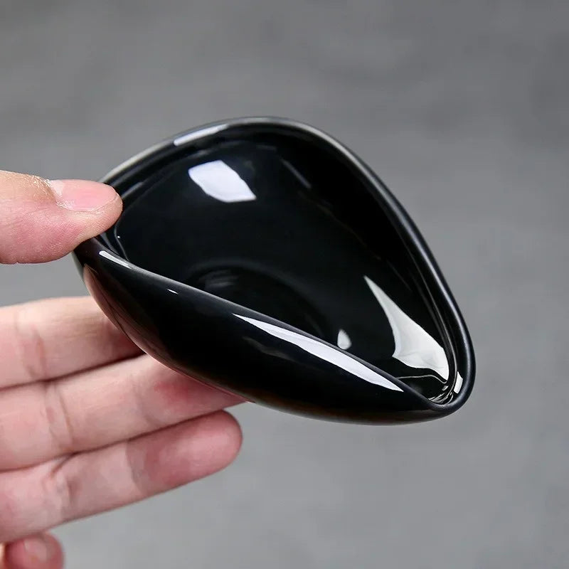 Hand holding a black ceramic espresso dosing cup with a wide spout and glossy finish