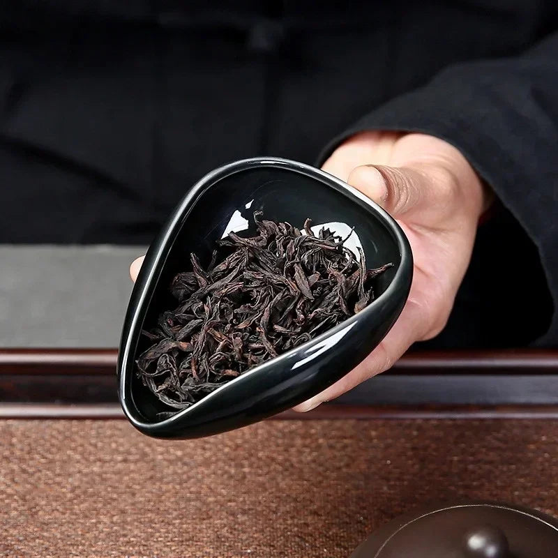 Hand holding a black ceramic bowl with loose leaf black tea, on a tea tray.
