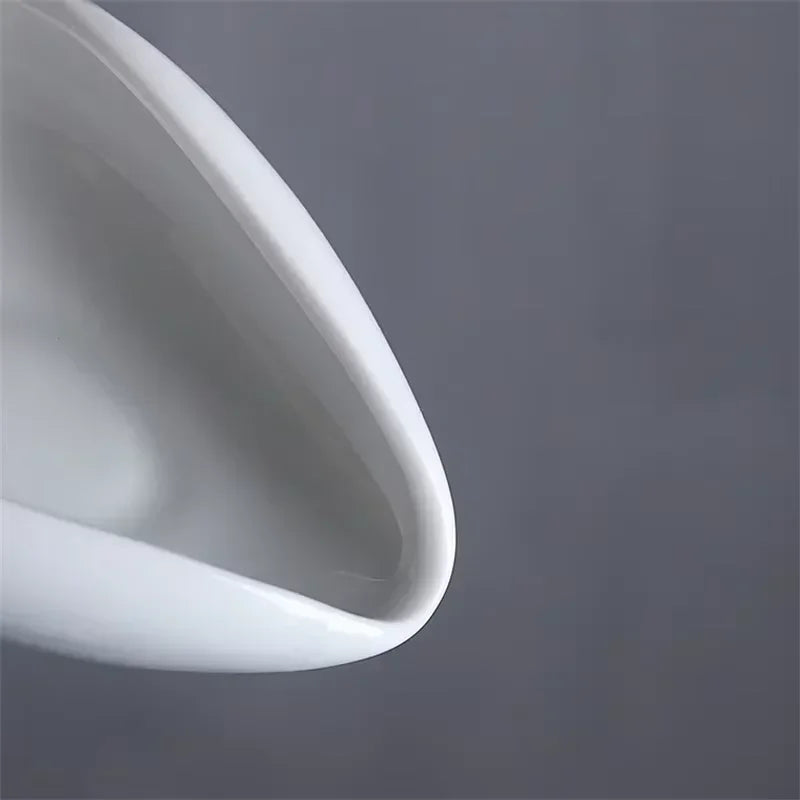 Close-up of a white ceramic espresso milk frothing pitcher spout on a gray background