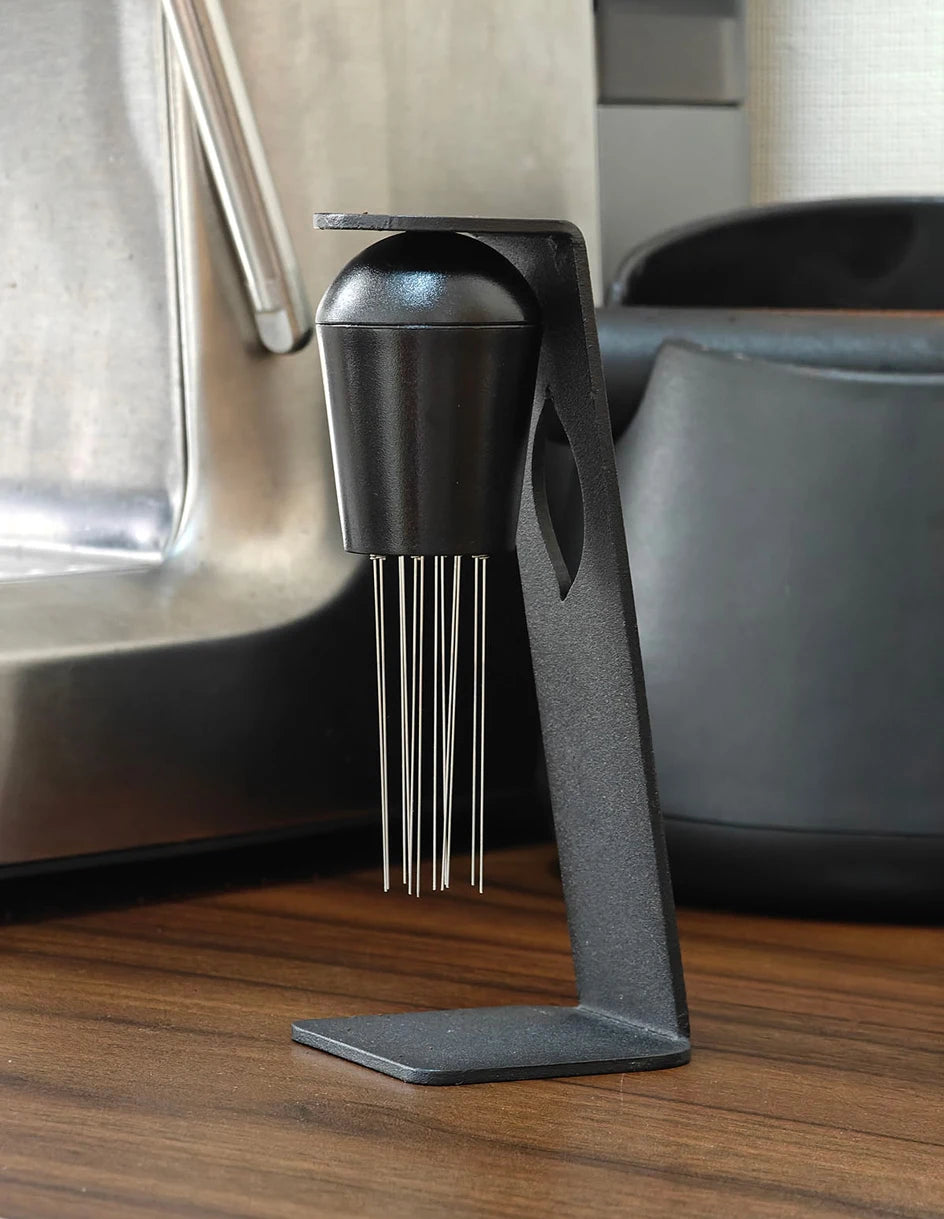Espresso distribution tool with stand on a wooden countertop next to coffee accessories