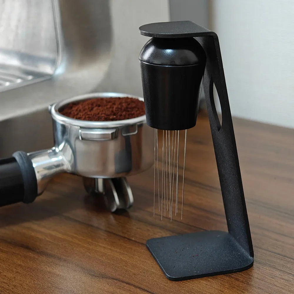 Espresso portafilter filled with ground coffee next to a coffee distribution tool on wooden counter