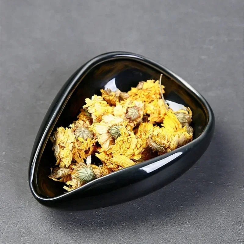 Dried yellow chrysanthemum flowers in black ceramic bowl on grey background