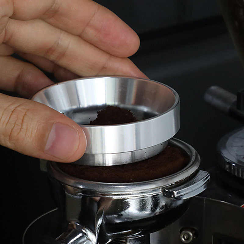 Hand placing a metal dosing ring on portafilter with fresh coffee grounds for espresso