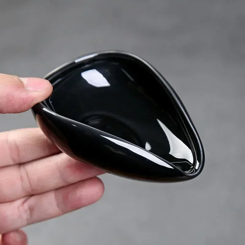 Hand holding a glossy black ceramic espresso dosing cup against a gray background