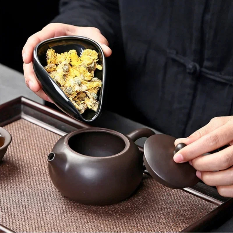 Person preparing loose leaf herbal tea in a ceramic teapot on a serving tray