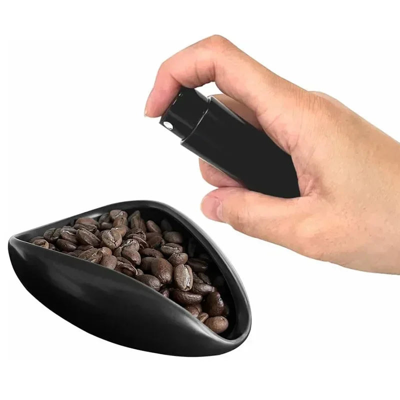 Hand using spray bottle over dish of whole coffee beans, home barista coffee accessory
