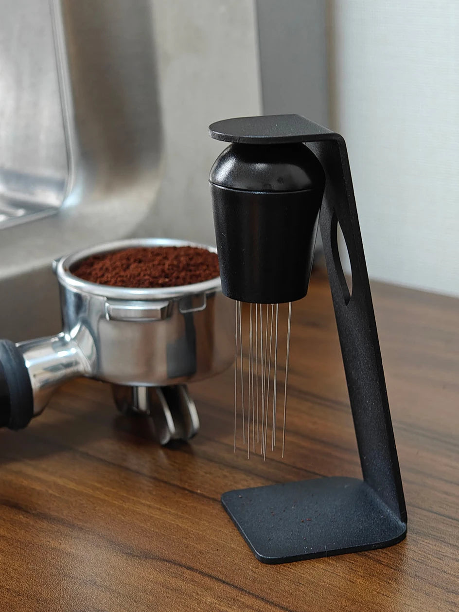 Espresso portafilter with coffee grounds beside a coffee distribution tool on wooden counter